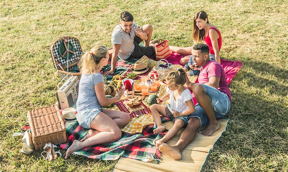 Group of people outside on picnic blankets having a picnic and safely eating their favorite healthy foods outside.