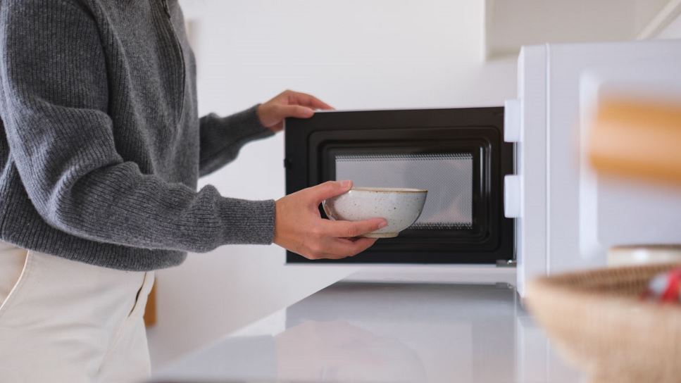 Close up of a hand putting a bowl of food into microwave