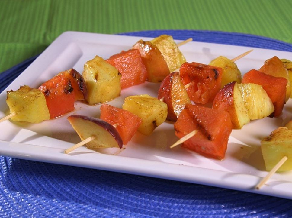 A white rectangular plate with four fruit kebabs containing grilled pineapple and watermelon.