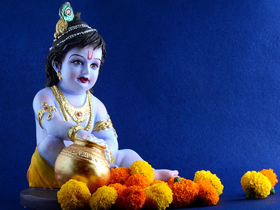 Hindu God Krishna sits with a butter pot and flowers to represent the Krishna Janmashtami celebration.
