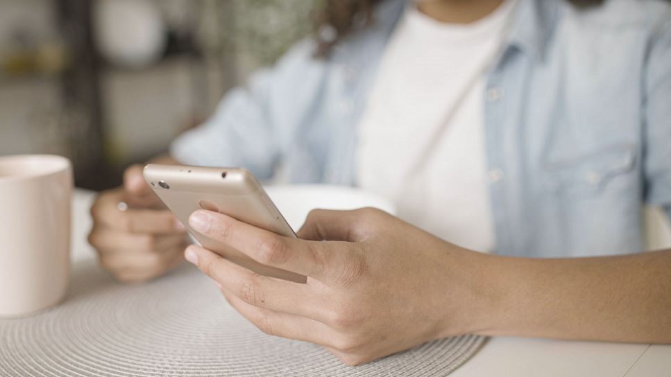 Close up of teenager's hand scrolling on cellphone while eating breakfast