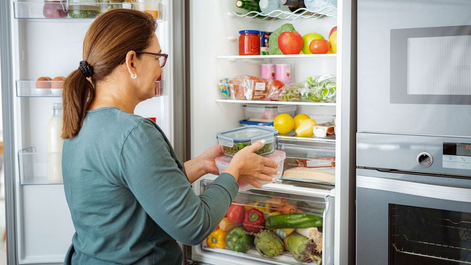 Woman putting leftover containers into an open refrigerator.