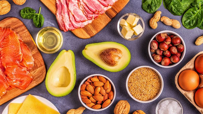 An assortment of high fat and low carbohydrate foods, including avocado, bacon, nuts, cheese, oil, butter and salmon.