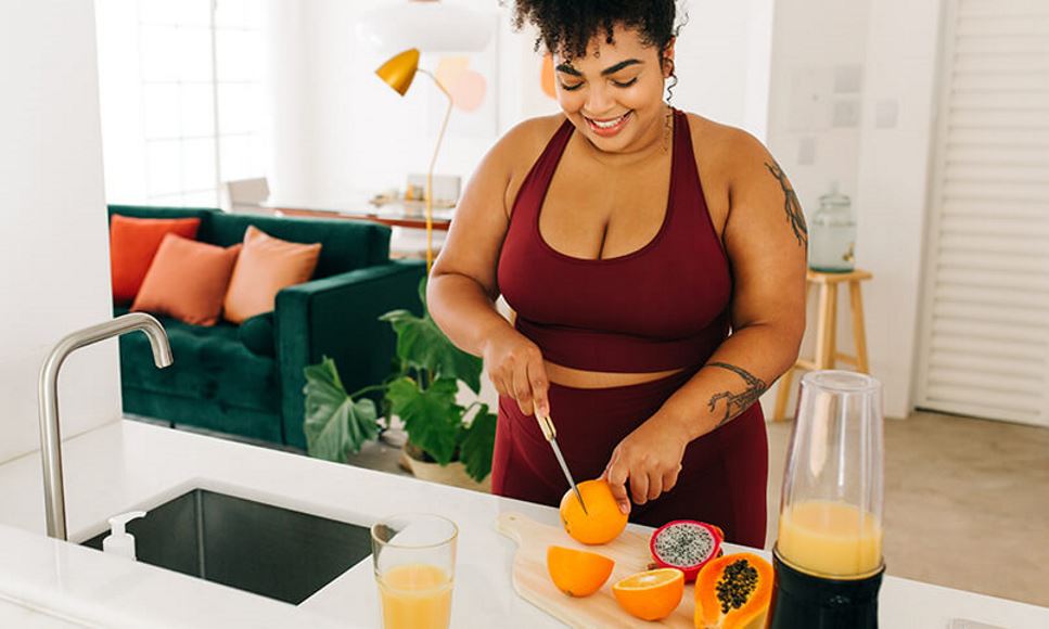 woman in workout clothes cutting fruit for smoothies