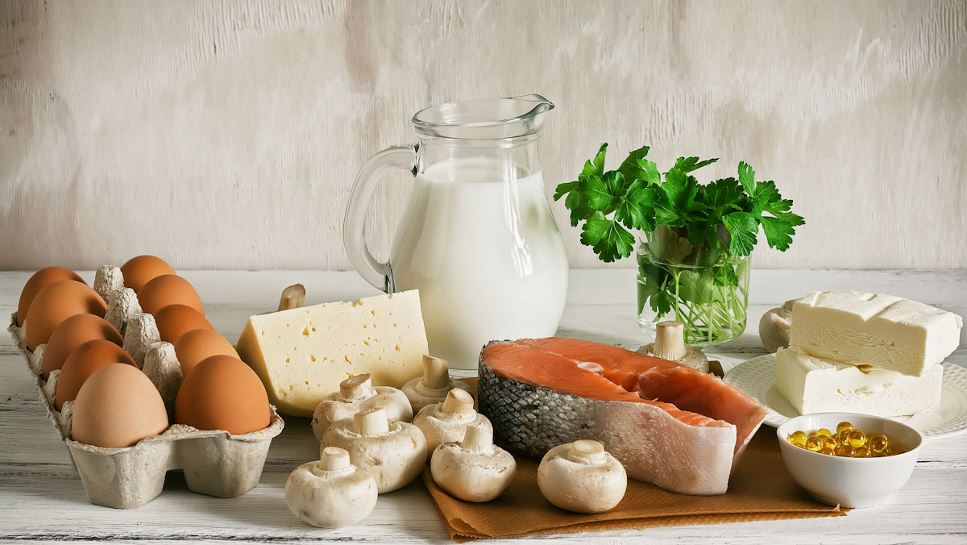 Assortment of foods providing vitamin D, including fortified milk and cheese, eggs, UV treated mushrooms and salmon.